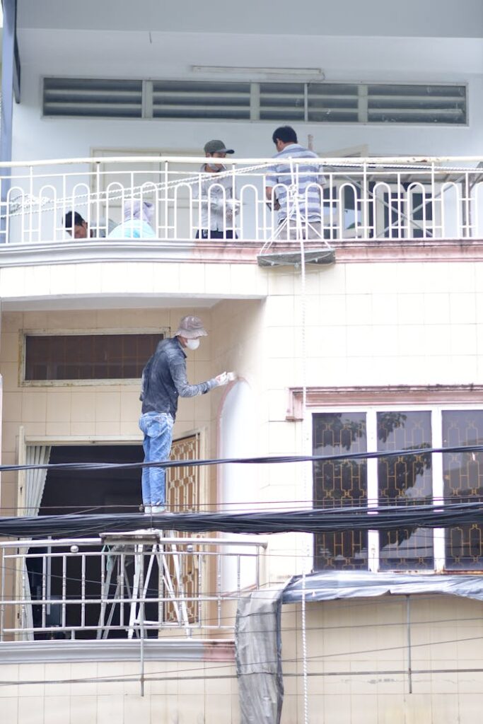 pexels photo 34264476 Construction workers painting and renovating a building facade, captured outdoors during daytime.