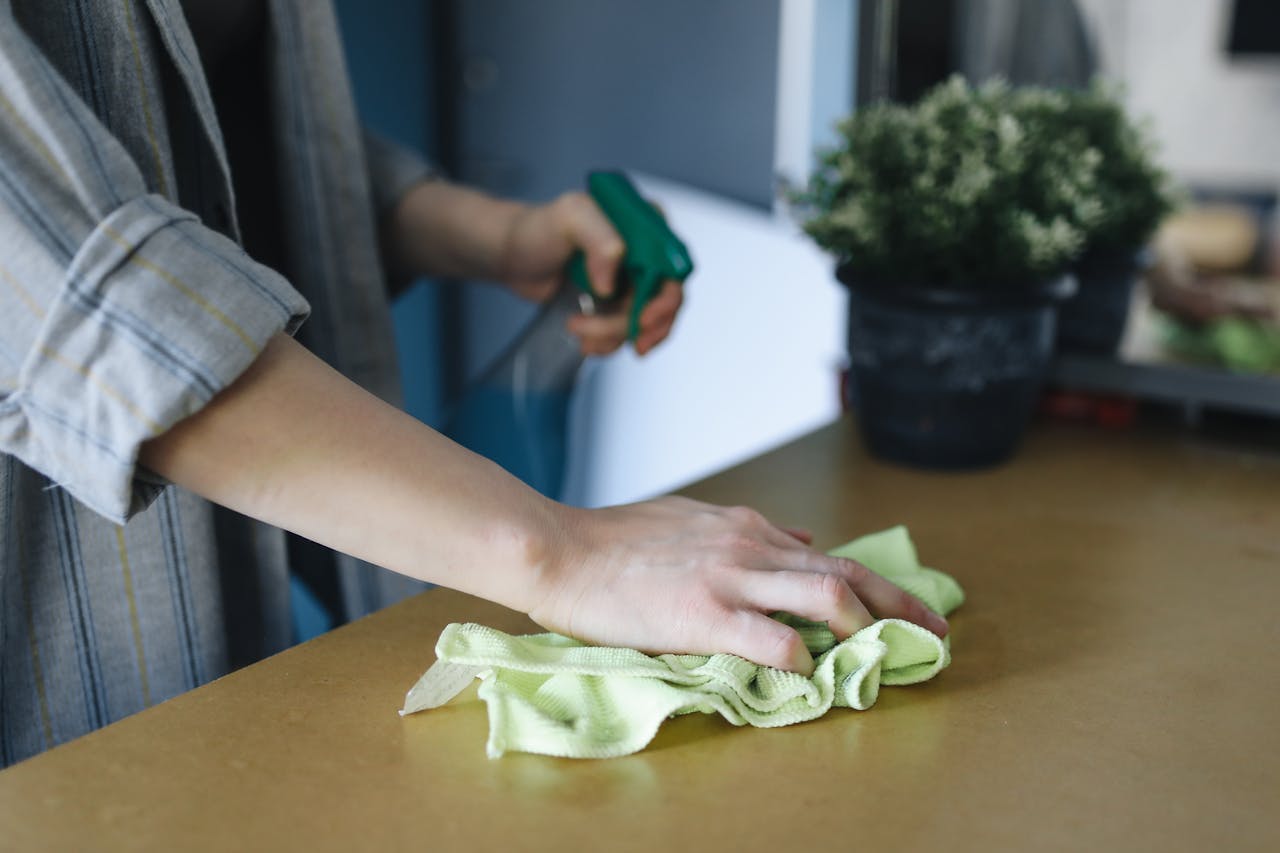 Home Close-up of a woman wiping a table with a spray bottle and cloth indoors, symbolizing effective housekeeping.