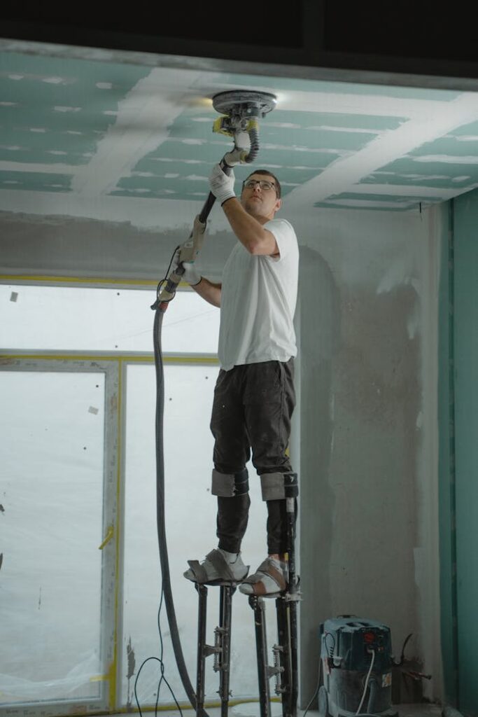 pexels photo 6474202 A man on stilts uses a ceiling sander for home renovation, focusing on drywall preparation.