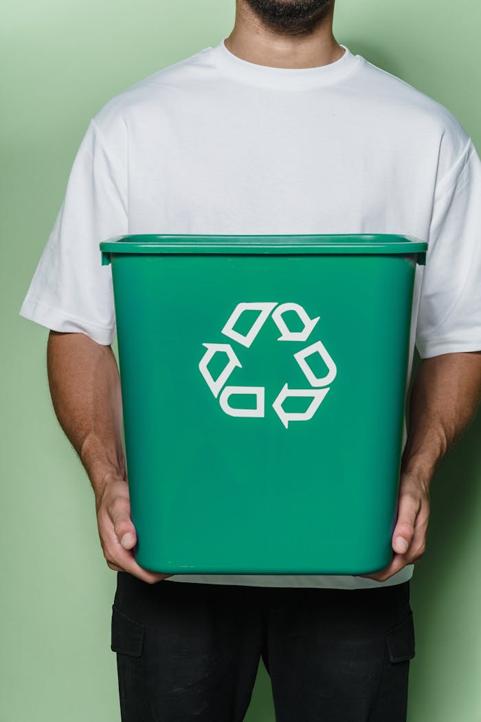 About Adult male holding a green recycling bin against a green background, promoting sustainability.